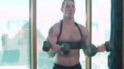 Tattooed man works out with weights and a submissive fella